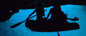 Załoga na pontonie wewnątrze błękitnej groty na wysepce Bisevo w Chorwacji. Światło słoneczne odbija się od dna i podświetla na niesamowity, błękitny kolor wodę w grocie.