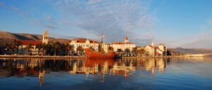 Zachód słońca nad starówką w Trogirze w Chorwacji. Widoczne odbicia statku i budynków w wodach zatoki