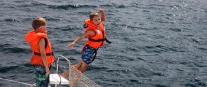 dziecie w kamizelkach ratunkowych skaczą dla zabawy z burty katamaranu podczas postoju w Zatoce Kotor w Czarnogórze