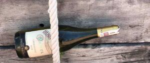 butelka wina Panul, zatknięta za żeglarską linę na tle starych desek. Rejs na życzenie w Hiszpanii.