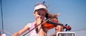 Młoda załogantka reju rodzinnego gra na skrzypcach na pokładzie katamaranu