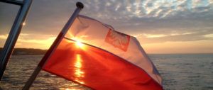 Polska bandera na tle zachodzącego słońca podczas rejsu na Morzu Bałtyckim
